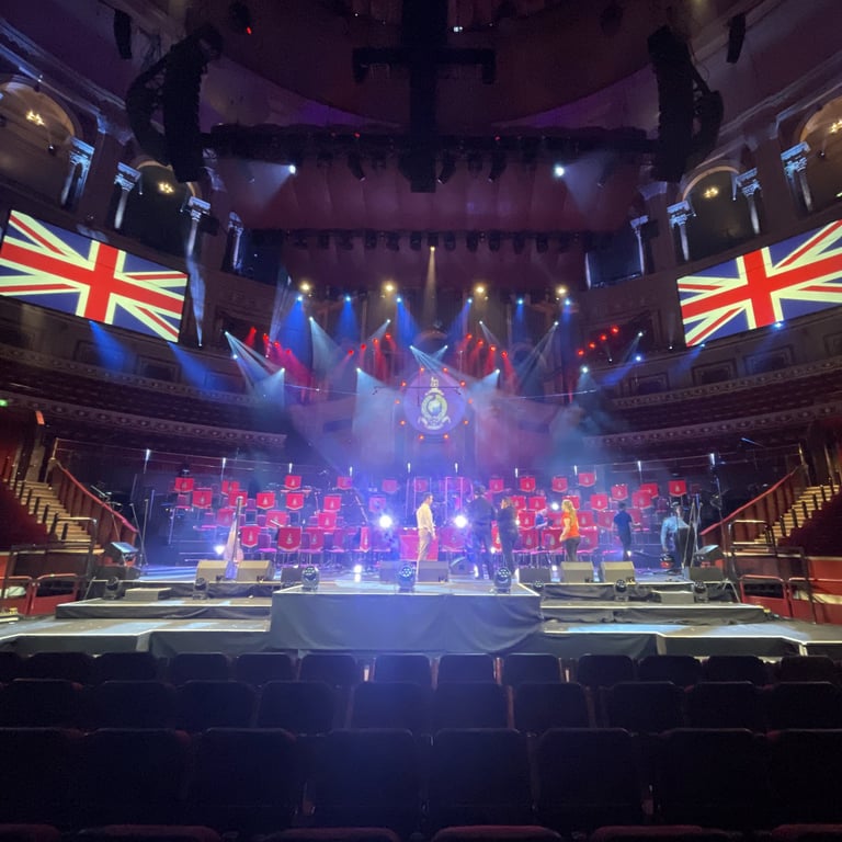 Union Jacks being projected either side of HM Royal Marines Massed Bands Orchestra on stage at the Royal Albert Hall London