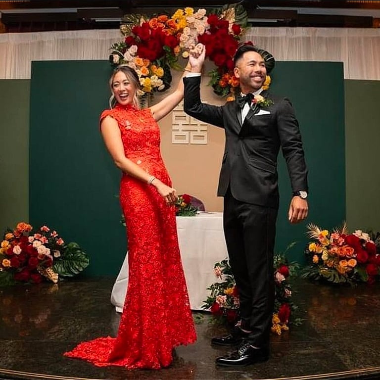 Romantic wedding moment featuring a smiling bride in a fitted red lace gown and a groom in a classic
