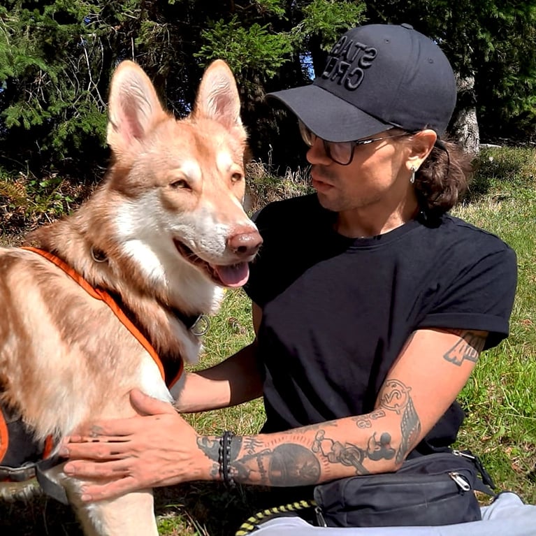 photo of a man wearing a black baseball cap and glasses sitting on the grass with a large brown dog