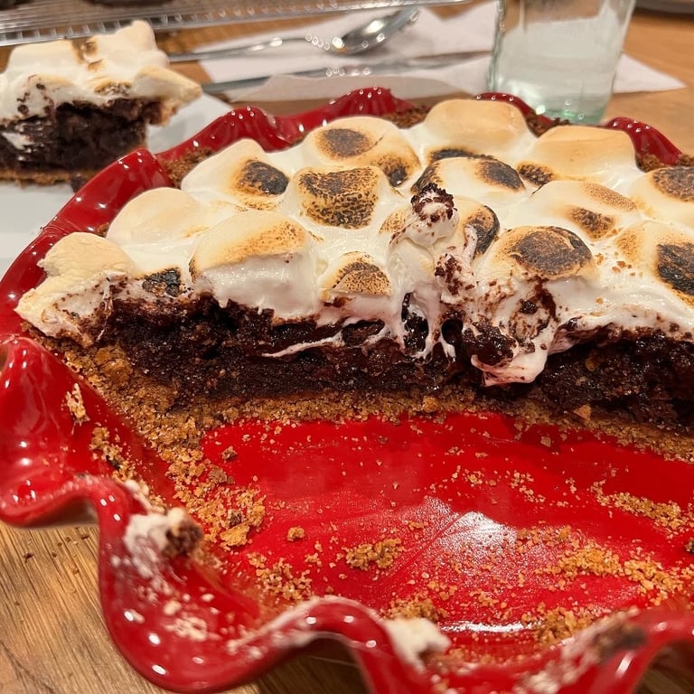 A homemade chocolate s'mores pie with toasted marshmallow topping in a red ruffled ceramic dish.