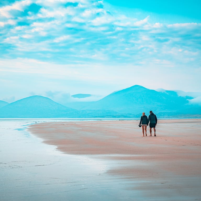 Un couple marche paisiblement sur la plage de Luskentyre, avec des montagnes brumeuses en toile de fond.