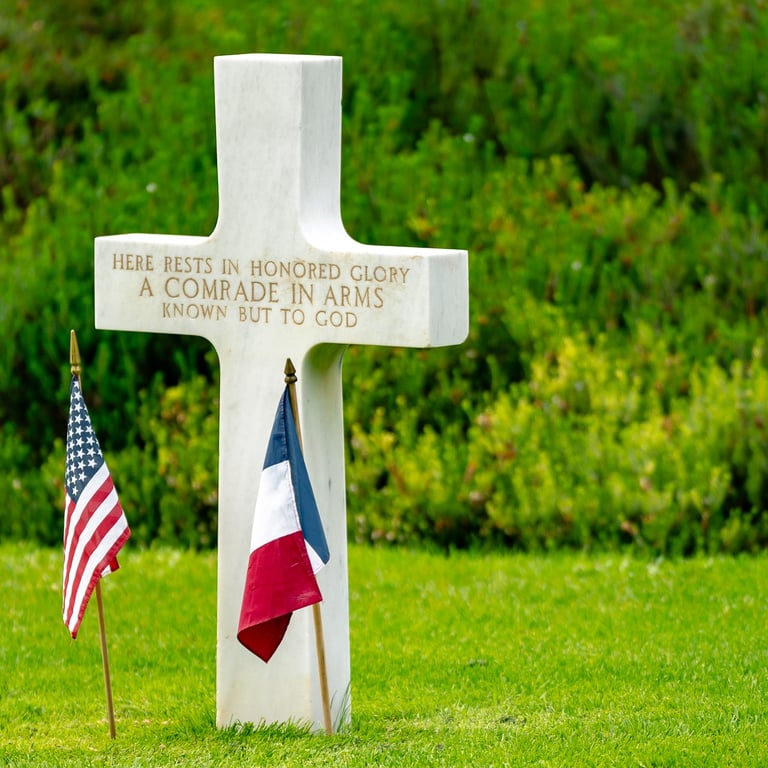 Tombe de soldat inconnu au cimetière de Colleville-sur-Mer, croix blanche avec inscription et drapeaux américain et français.