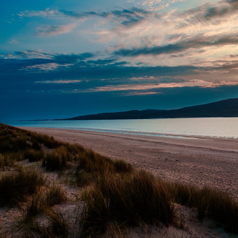 Coucher de soleil sur Luskentyre, le ciel se teinte d'ombres bleues et d'oranges doux, illuminant l'océan calme et les dunes.