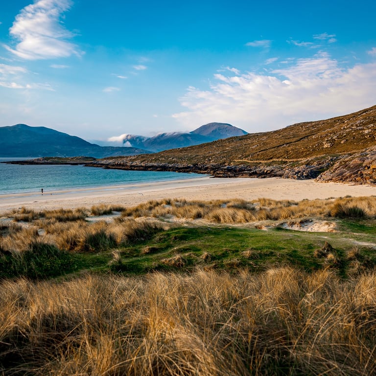 Plage de Luskentyre, dunes dorées et eaux turquoise, entourées de montagnes calmes sous un ciel dégagé.