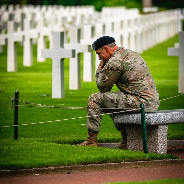 Soldat en uniforme de camouflage assis sur un banc dans un cimetière militaire, exprimant tristesse devant des croix blanches