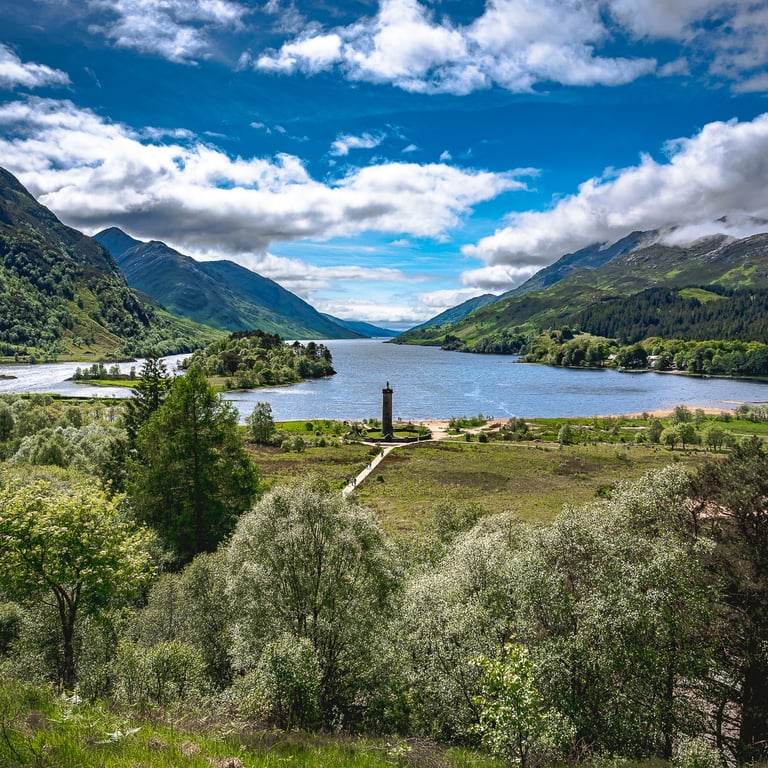 Vue panoramique du Loch Shiel depuis le viaduc de Glenfinnan, entouré de montagnes verdoyantes et d'un ciel lumineux.