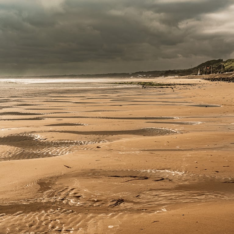 Plage d'Omaha Beach sous un ciel nuageux. Le sable doré et calme contraste avec l'histoire tragique du Débarquement.