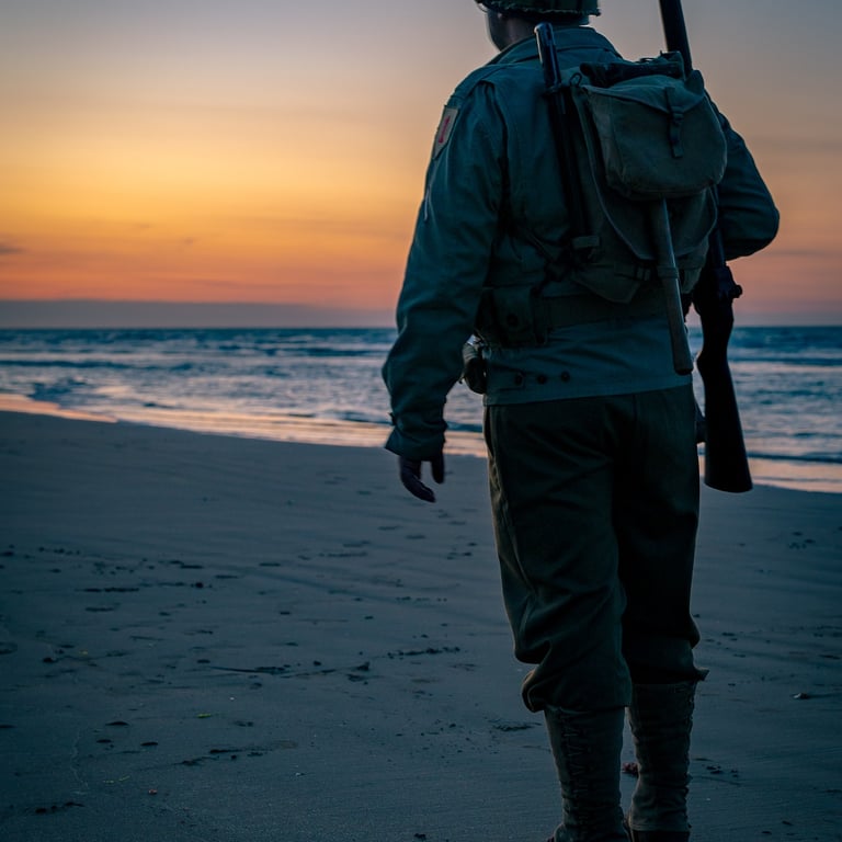 Soldat en uniforme sur Omaha Beach au crépuscule, regard tourné vers l'horizon. Coucher de soleil doré, calme et tension.