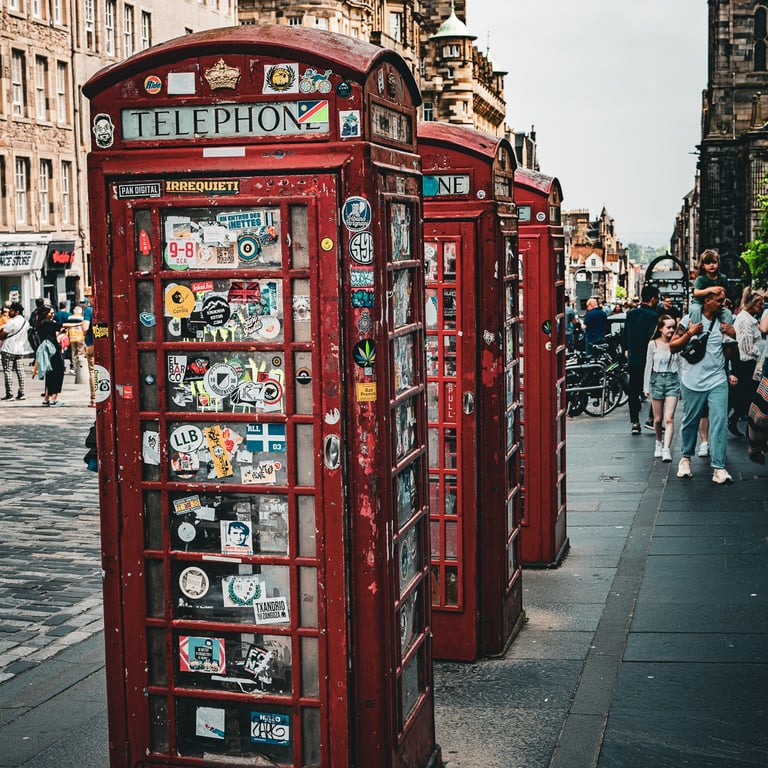 Cabines téléphoniques rouges emblématiques, couvertes de stickers, alignées dans une rue animée d’Édimbourg.