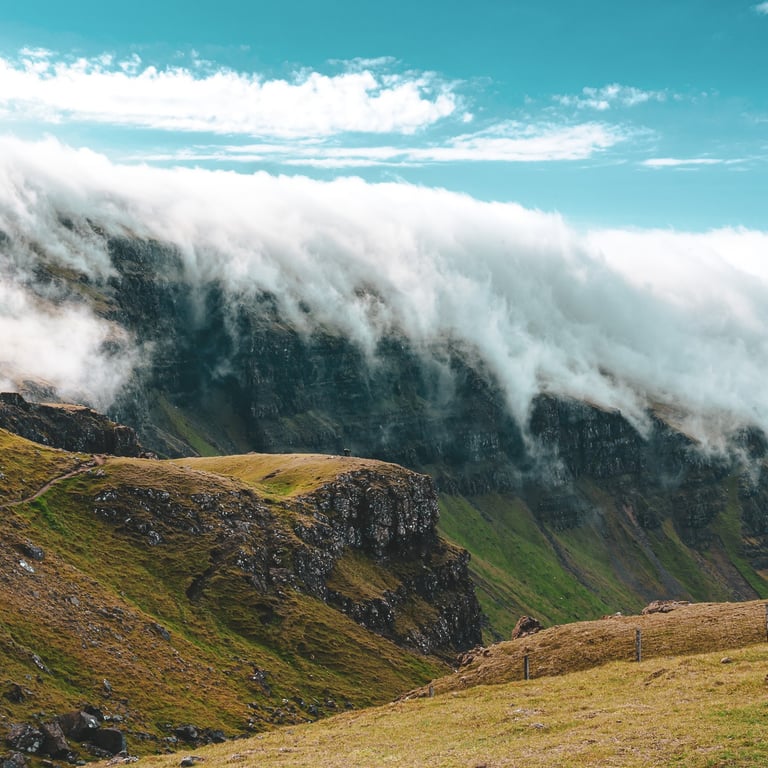 Une chaîne de montagnes verdoyantes enveloppée de nuages épais, sous un ciel bleu clair, offrant un paysage majestueux.