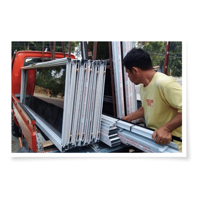 Two men unload glass display cases from a truck under a tree-lined street, preparing them for installation or transport.