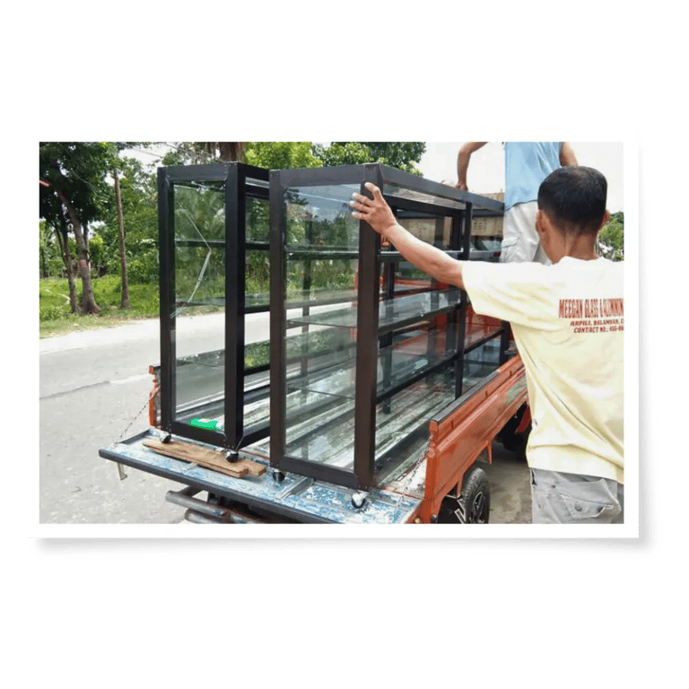 A worker loads several aluminum window frames onto a pickup truck in a sunny outdoor setting.