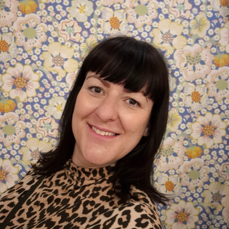 a woman with dark hair and a fringe wearing leopard print standing against a floral background