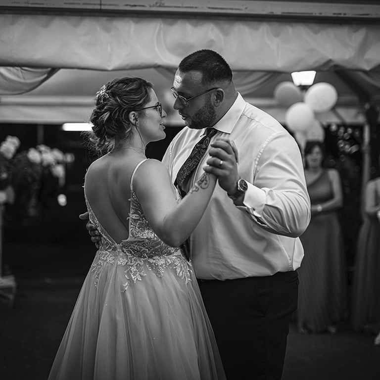 Ein Schwarz-Weiß-Foto eines Brautpaares, das bei seiner Hochzeit tanzt, wobei die Braut ein rückenfreies Kleid trägt und der 