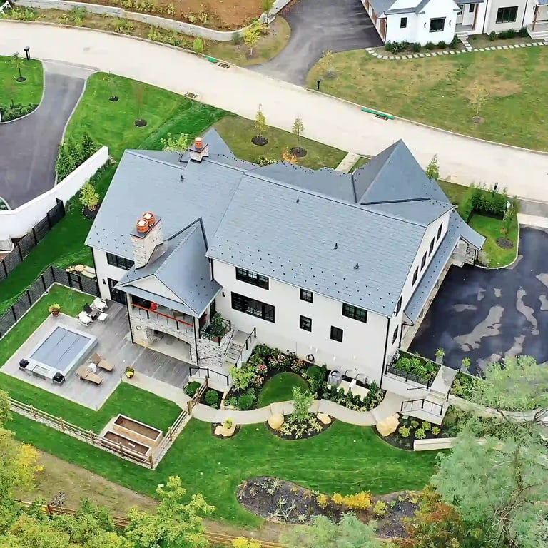 Aerial view of a luxury home's backyard with patio, hot tub, and landscaped lawn for real estate listing
