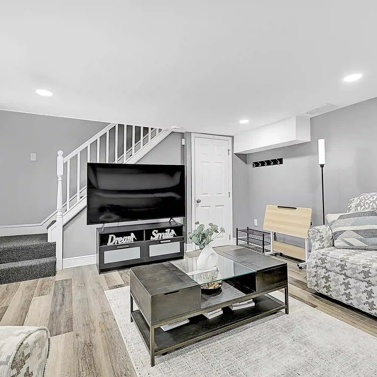 Stylish modern basement living room in a Philadelphia short-term rental with TV, gray walls, and hardwood-style flooring