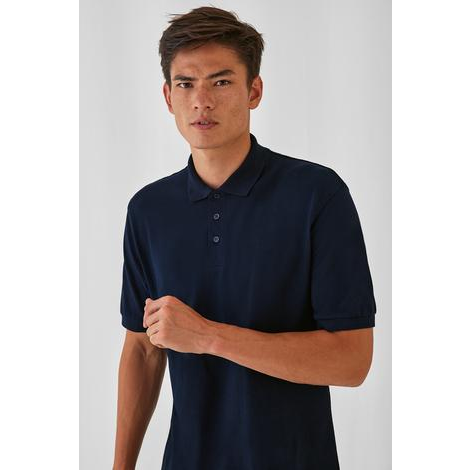 a man in a blue shirt and jeans standing in front of a white wall