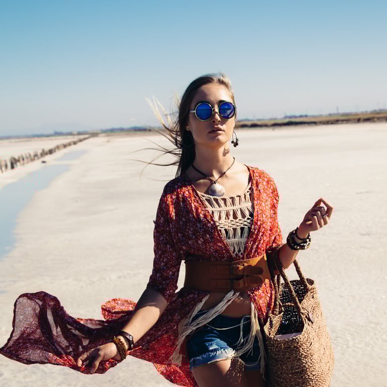 a woman in a red dress and sunglasses walking on a beach