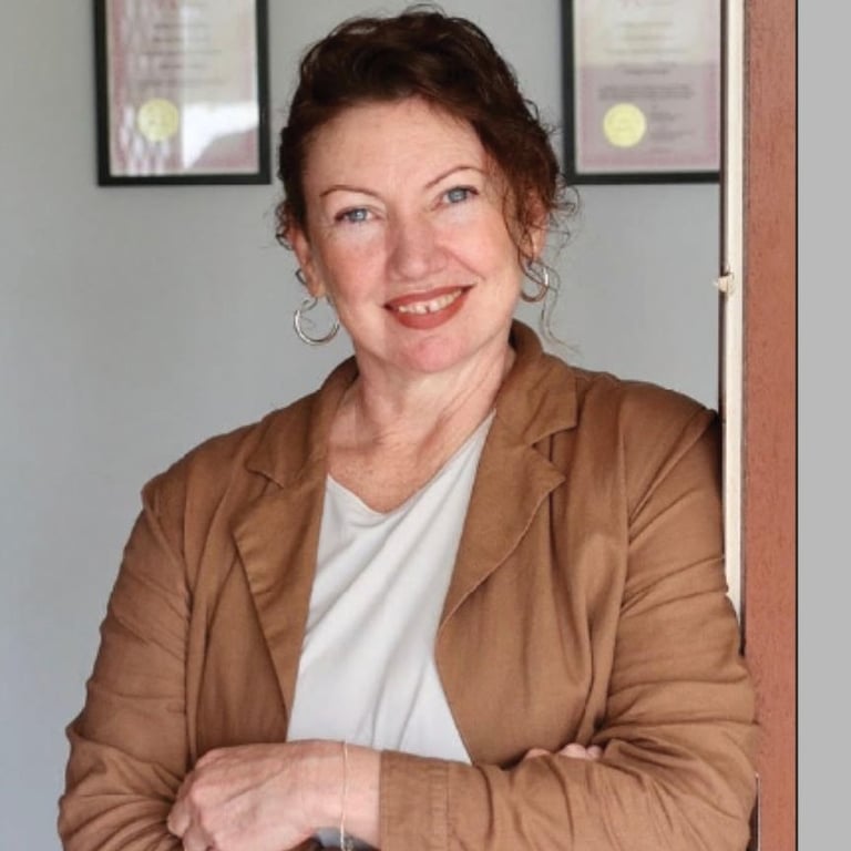 A smiling professional woman with curly dark hair wearing a brown blazer leaning against a doorway.