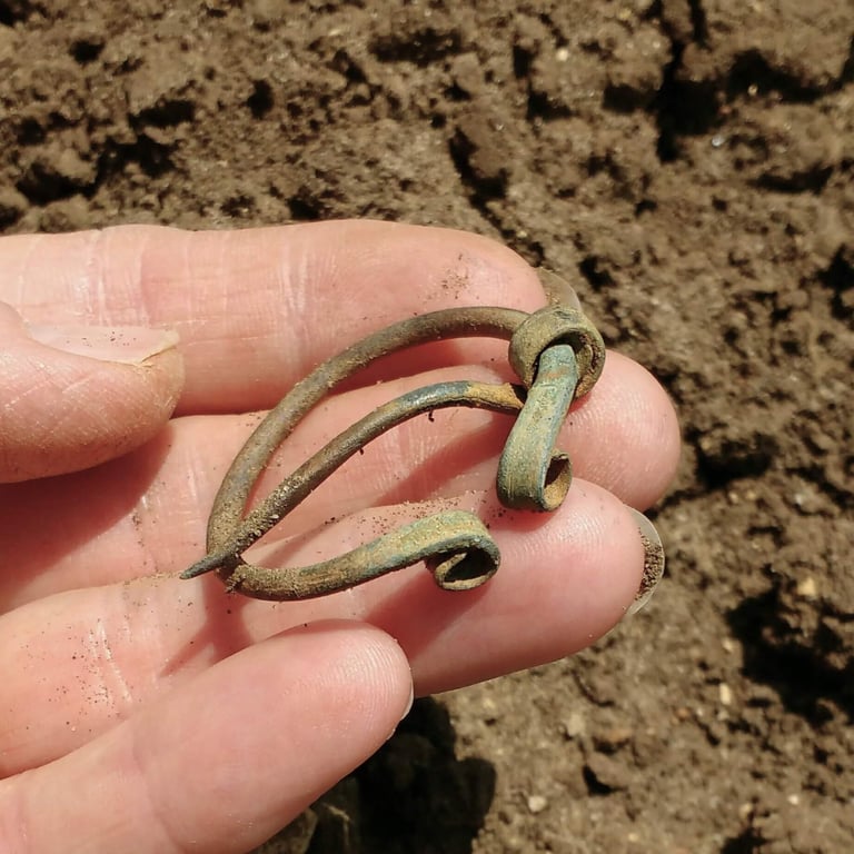 A bronze, circular Iron Age brooch held in the hand of the finder.
