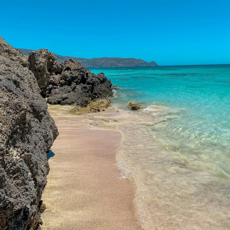 A scenic view of Elafonissi Beach with pale pink-tinged sand and clear turquoise shallow waters