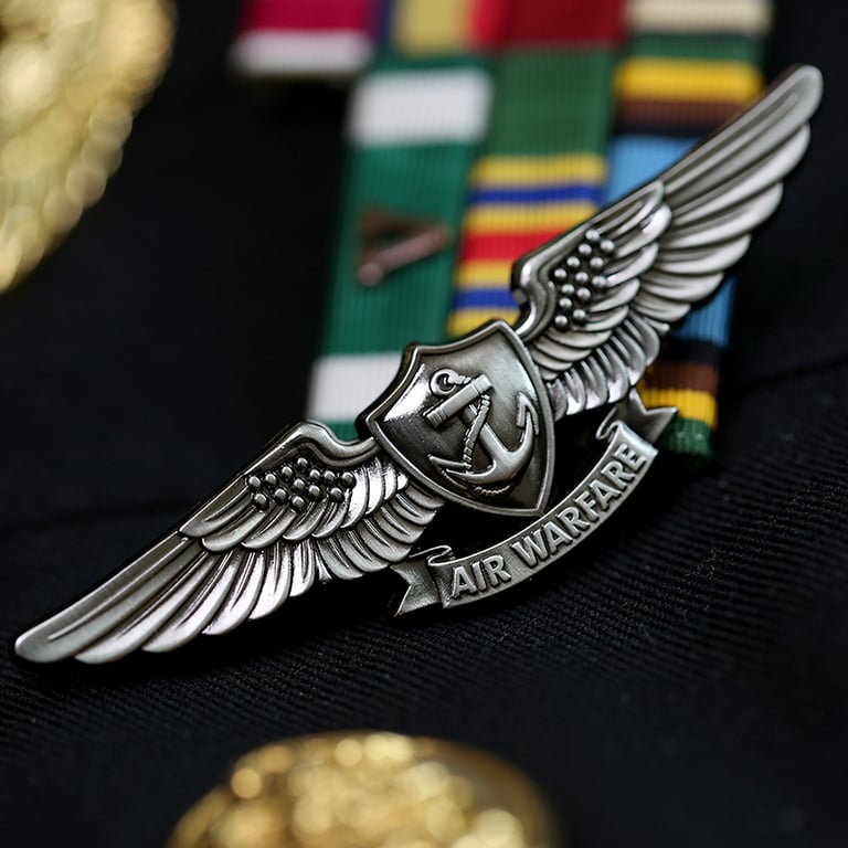 Silver Enlisted Aviation Warfare Specialist insignia pin on a US Navy uniform with ribbons.