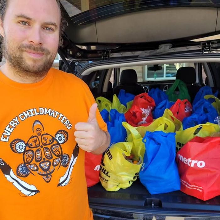 A smiling founding member beside a van trunk filled with donated food items