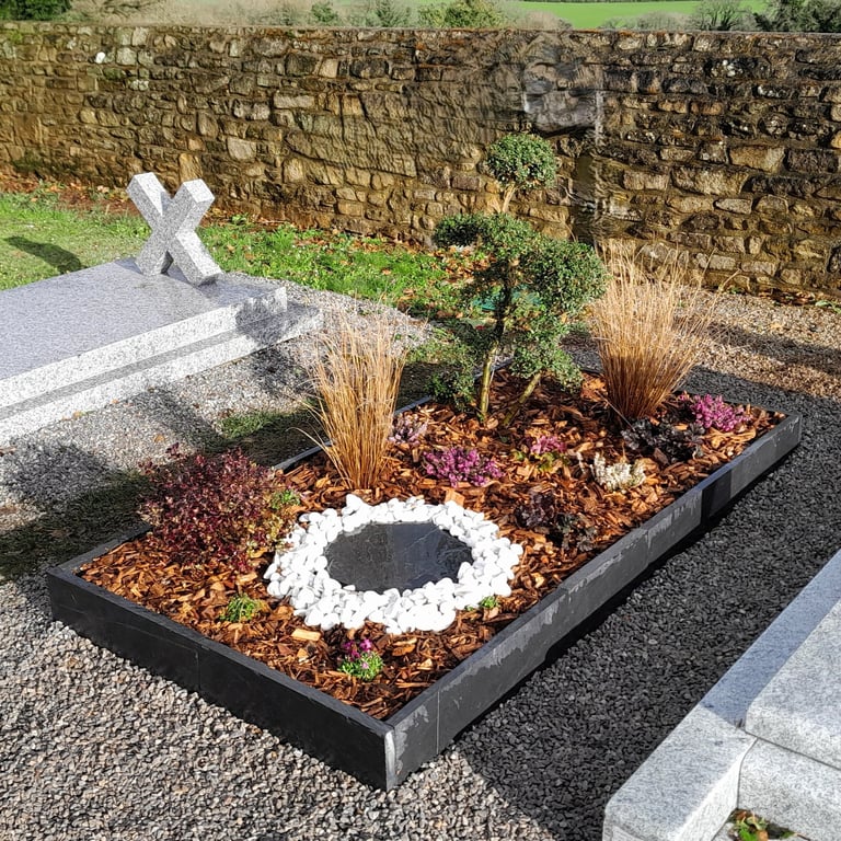 Sépulture moderne avec cadre en schiste, cercle de pierres blanches et paillis naturel.
