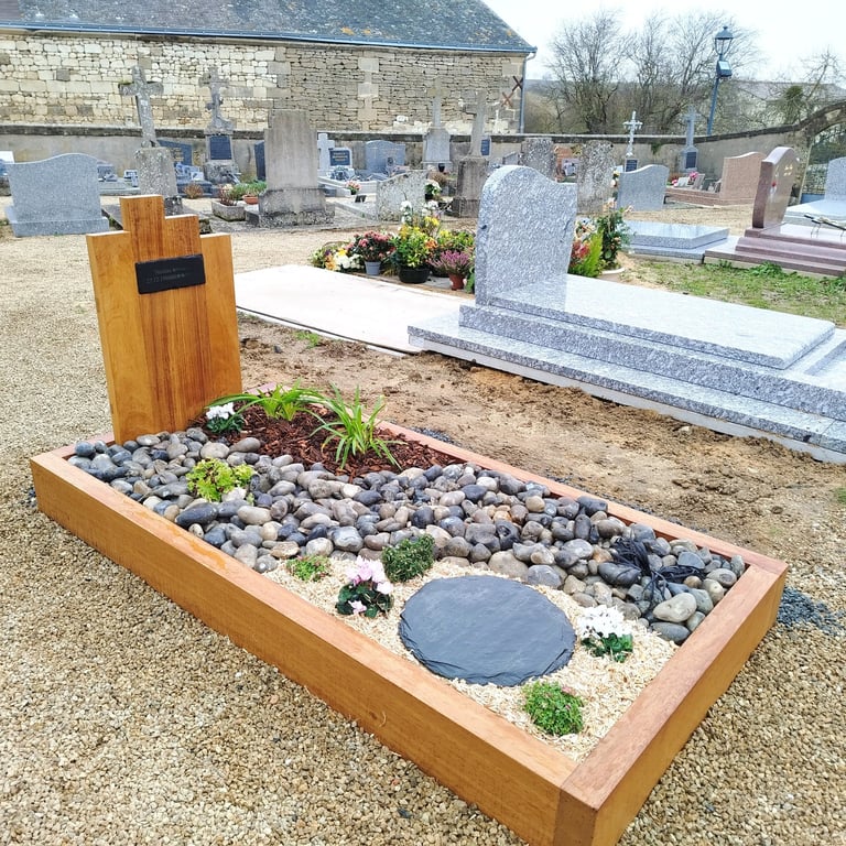 Aménagement funéraire avec encadrement bois, galets gris, schiste et fleurs de saison.