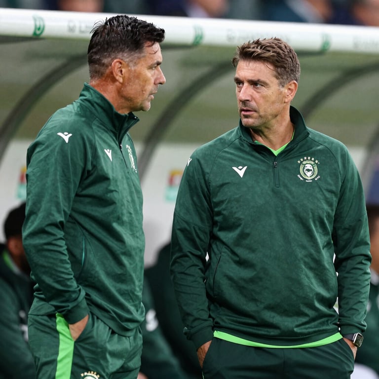 Two coaches in deep conversation on the sidelines of a professional match, wearing branded forest green gear, serious and strategic mood.