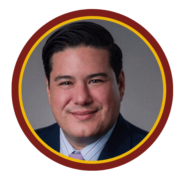 Professional headshot of a smiling man in a suit, framed in a circular maroon and gold border. Mike