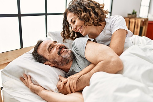 A joyful middle-aged man and woman with curly hair laughing and embracing while lying in bed