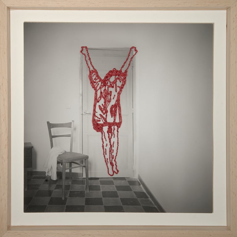Conceptual art photo of a red beaded human figure hanging over a door in a minimalist room.