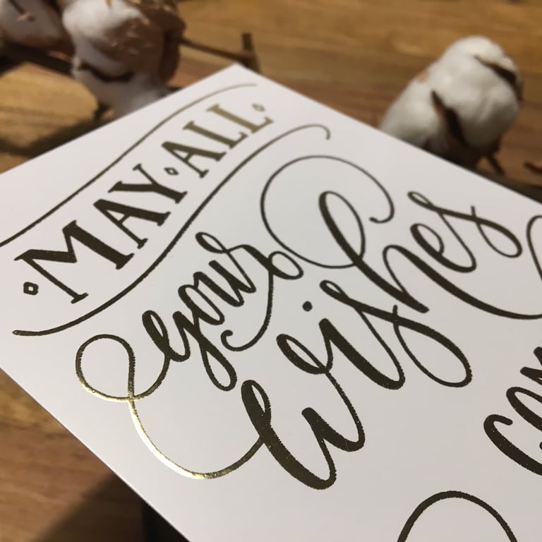 Elegant gold foil greeting card with handwritten calligraphy saying May All Your Wishes Come True.