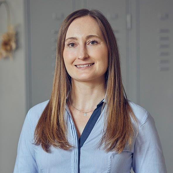 Professional portrait of a smiling woman with long brown hair wearing a light blue button-down shirt.
