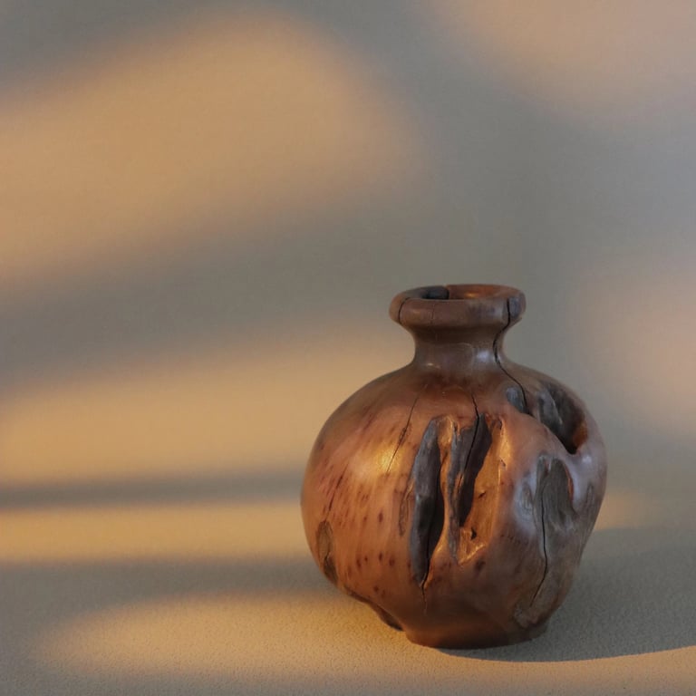 Handcrafted rustic wooden vase with natural bark texture and warm sunlight shadows.