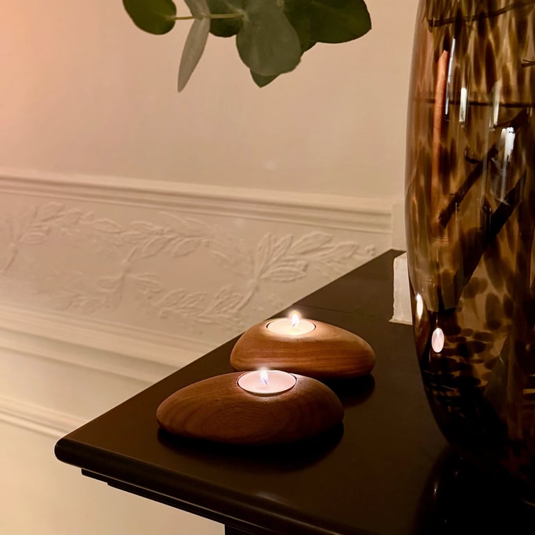 Two wooden pebble-shaped tea light candle holders on a dark table creating a cozy home atmosphere.