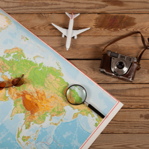 Travel planning flat lay with a world map, vintage camera, model airplane, and magnifying glass on wood.