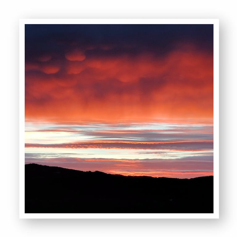 Stunning sunset sky with vibrant red, orange, and dark blue clouds above a silhouetted mountain range, enhancing