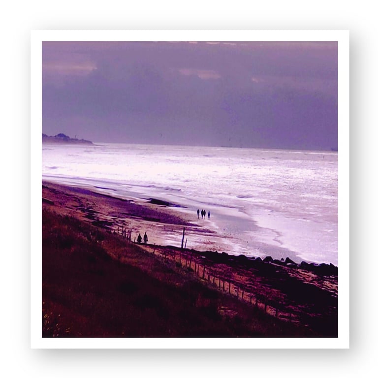 Silhouetted people walking on a sandy beach at sunset under a purple sky with ocean waves.