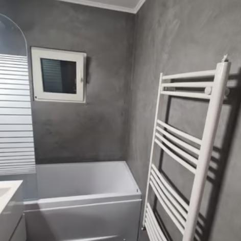 Modern bathroom featuring gray microcement walls, a white bathtub, and a wall-mounted heated towel rack.