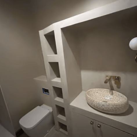 Modern bathroom with a stone washbasin, gold-coloured tap, built-in shelves and a wall-hung toilet,