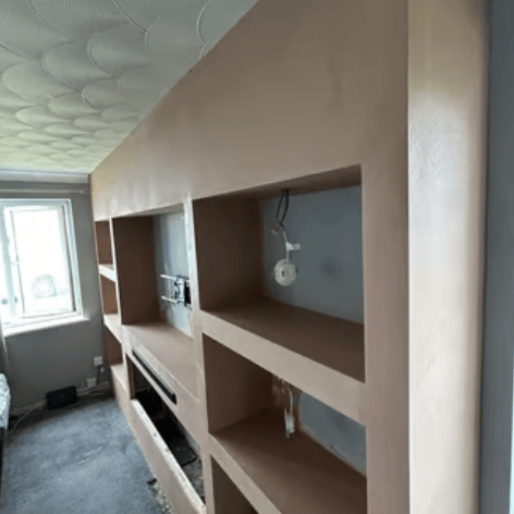 Freshly plastered media wall with recessed shelving and built-in electric fireplace frame.