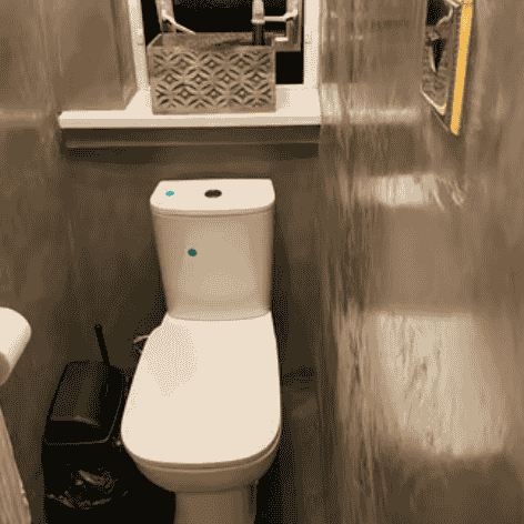 A modern white dual-flush toilet in a compact bathroom with grey textured walls and decor.