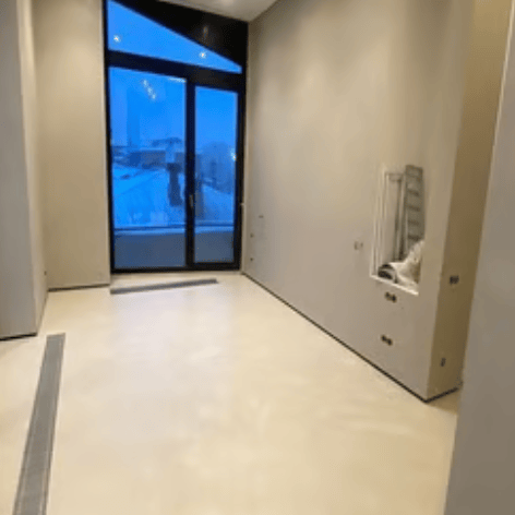 Modern empty room undergoing renovation, with microcement flooring and large glass doors leading to