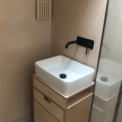 Modern, minimalist bathroom finished with microcement, featuring a white washbasin, black wall-mount