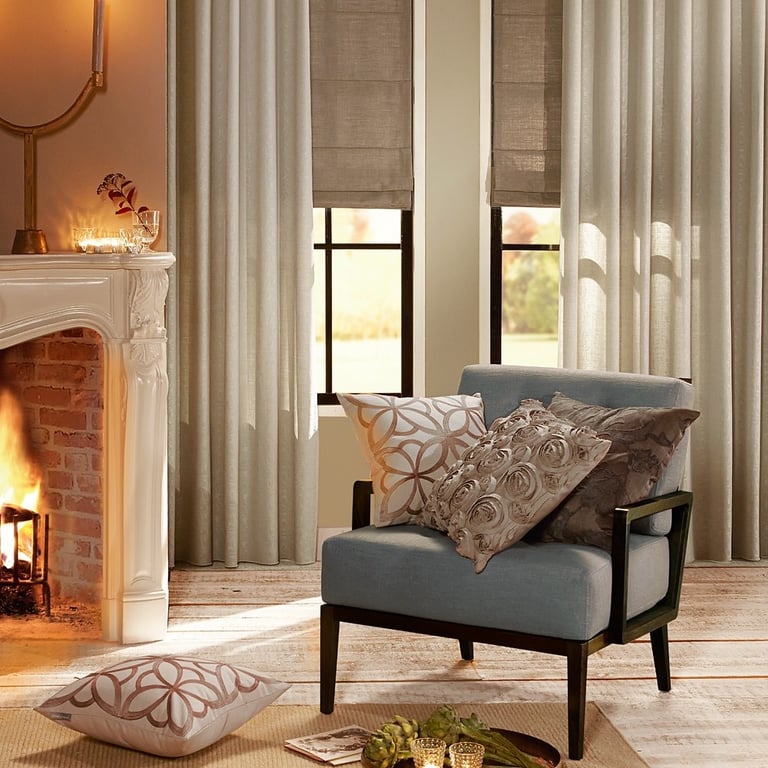 Elegant living room featuring linen drapes, roman shades, and a blue armchair by a fireplace.