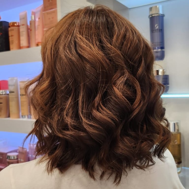 Back view of a woman with shoulder-length wavy auburn hair in a salon setting.