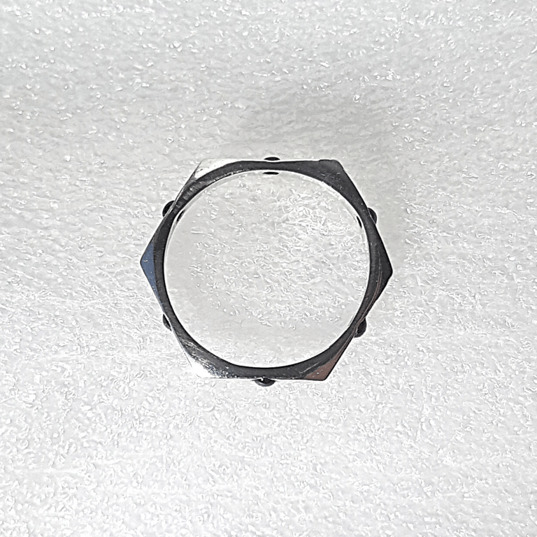 A hexagonal sterling silver ring, featuring six small black gemstones, sits on a white textured surface.