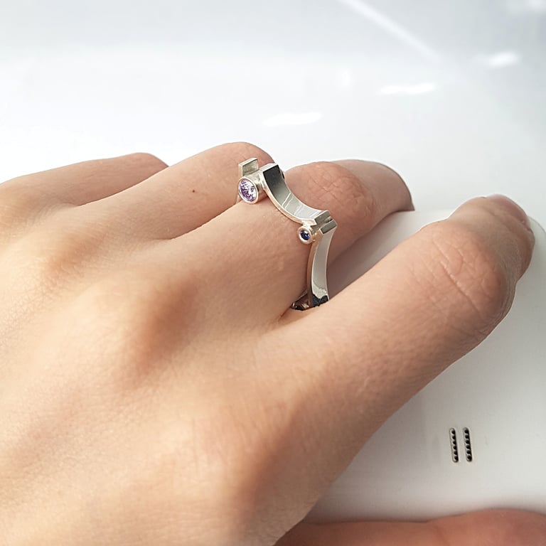 Hand wearing a unique sterling silver geometric ring with amethyst and sapphire stones.